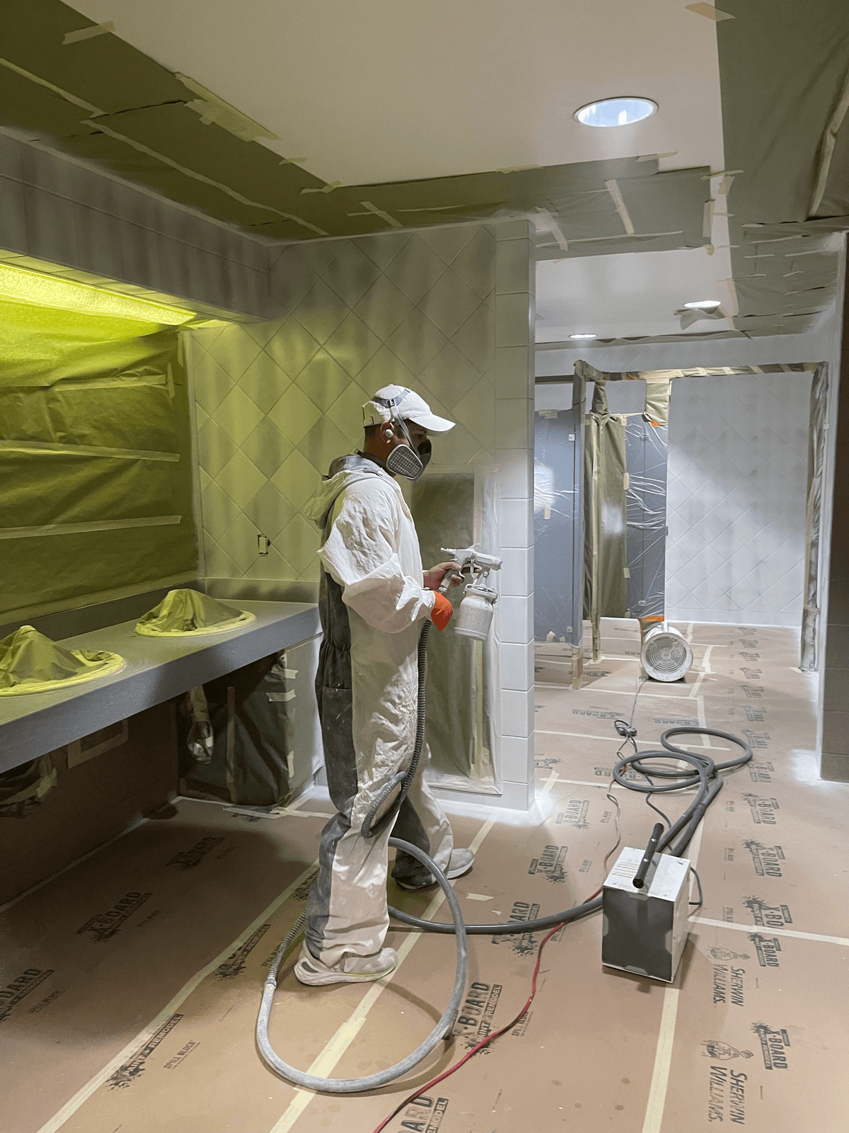 Technician in protective suit spray-refinishing a bathroom