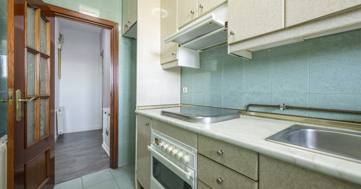 Closeup of an outdated kitchen with laminate countertops, old appliances, and a mint tile backsplash.