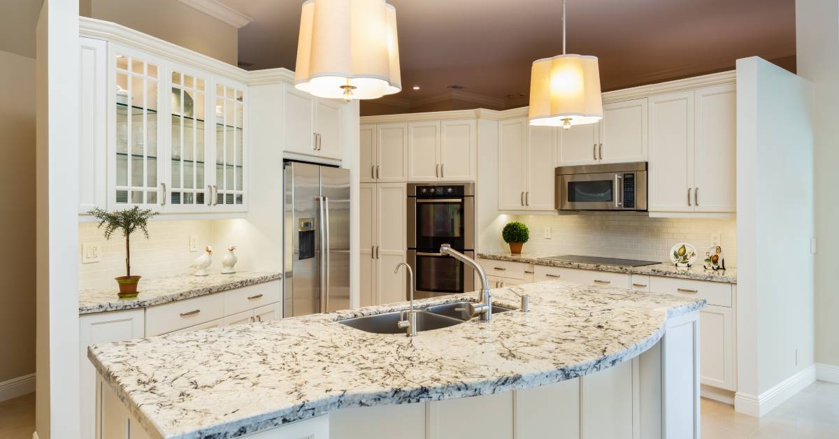A modern, open-concept kitchen with white cabinetry, granite countertops, a large island, and hanging lights.
