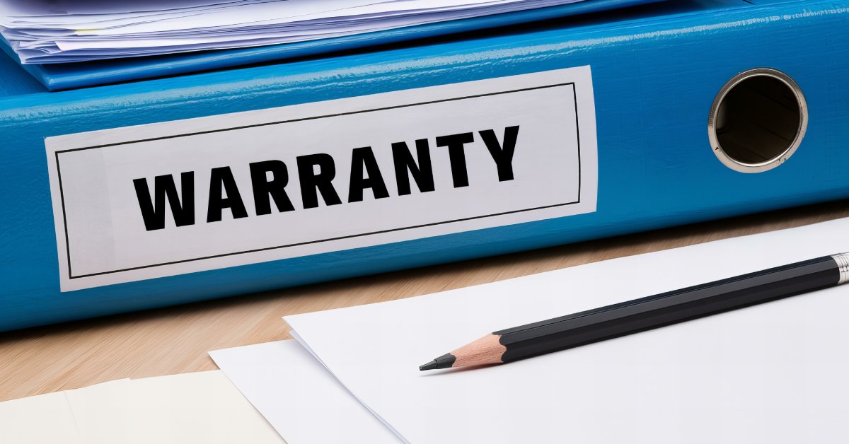 Close-up of a blue binder that says “warranty” on the side in black letters and sits next to a paper and pencil.