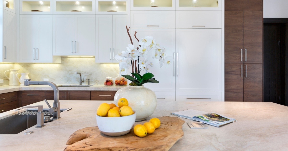 An upscale modern kitchen with white cabinets and a large center island with a vase of orchids and a bowl of lemons.