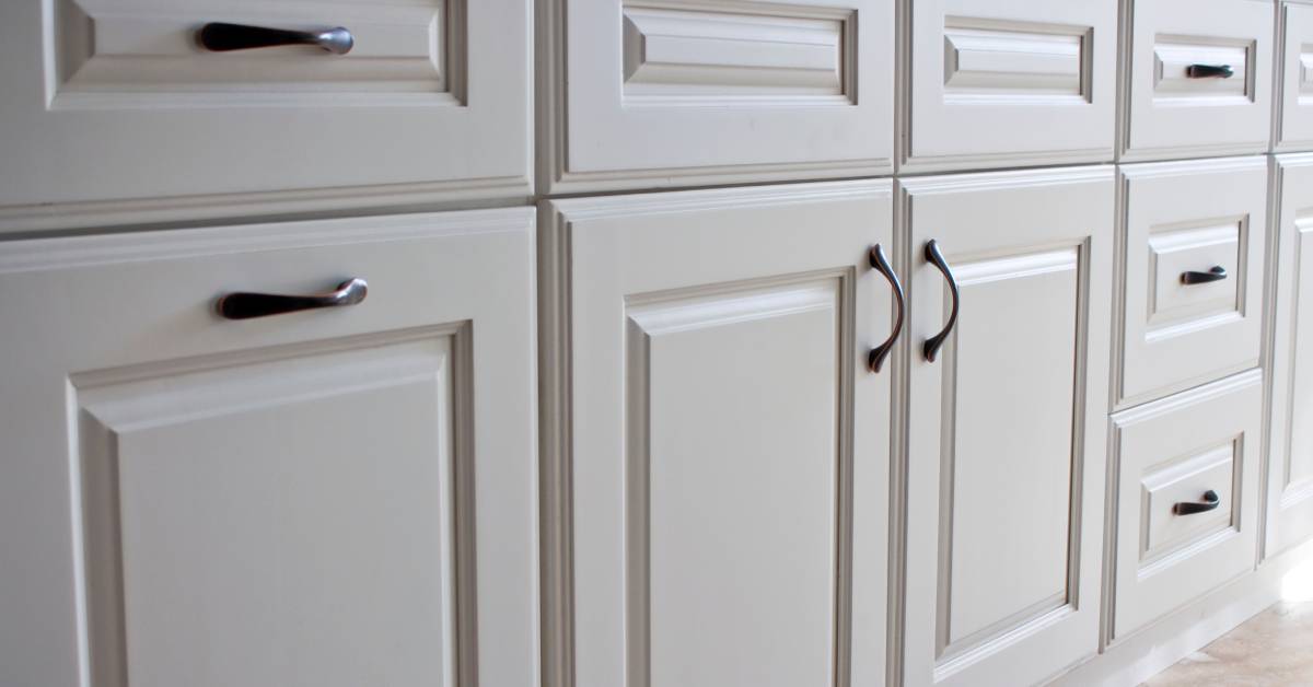 Closeup of several white cabinets and drawers with traditional Shaker-style faces and dark-colored hardware.