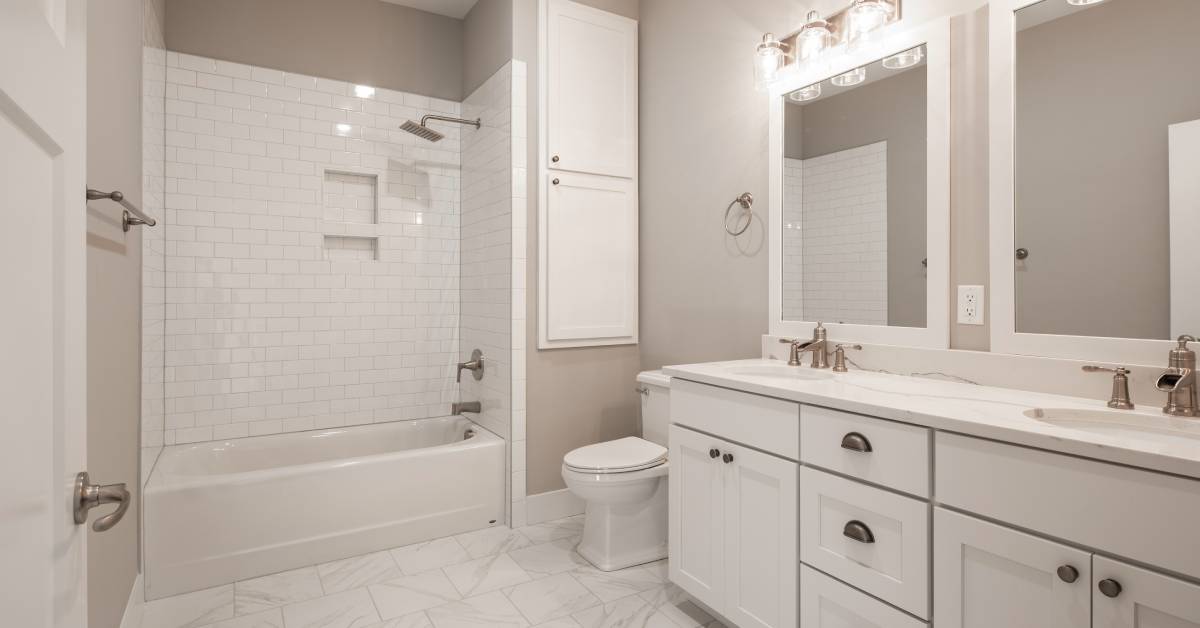 A white modern bathroom with a bathtub, toilet, double vanity, and cabinets that have been newly finished.