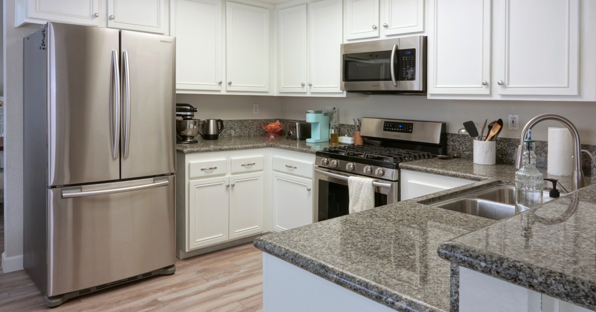 A modern, open-concept kitchen with stainless steel appliances, granite countertops, and white cabinets.