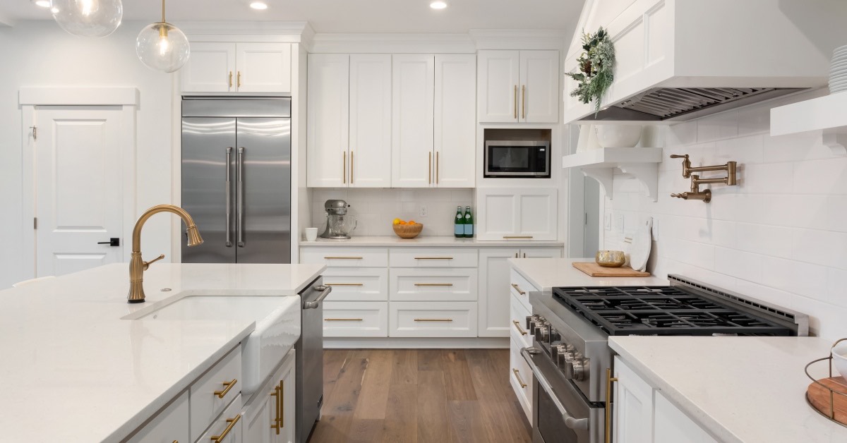 A modern kitchen with white cabinets, an island, stainless steel appliances, brass hardware, and light wood flooring.