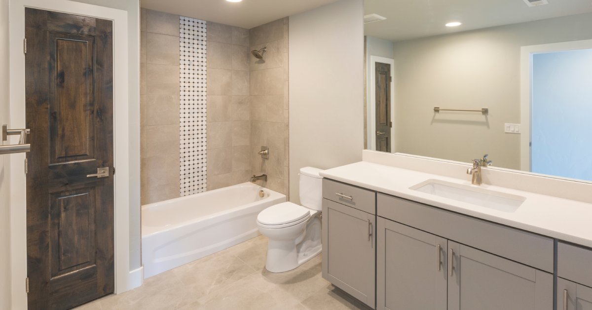 A new modern bathroom with a tub, a dark wood-stained closet, tile floors, a toilet, and a large vanity and mirror.